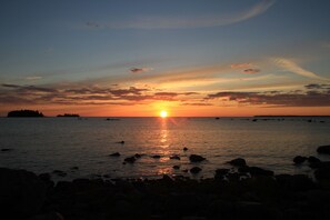 A sunset over a calm sea with rocks in the foreground.