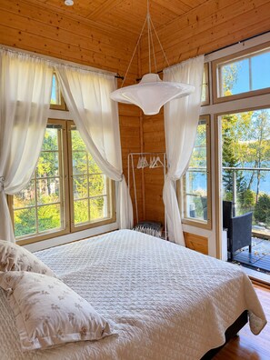 A bedroom with a large bed, a hanging light fixture, and a view of the outdoors. - Seaside Villa with jacuzzi and own beach (Maksamaa (Vöyri))
