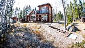 A large wooden cabin with a balcony, surrounded by trees and a gravel path leading to the entrance. - Seaside Villa with jacuzzi and own beach (Maksamaa (Vöyri))