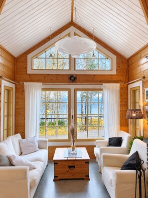 A log cabin interior with a high ceiling, two large windows, a central table, and two sofas. - Seaside Villa with jacuzzi and own beach (Maksamaa (Vöyri))