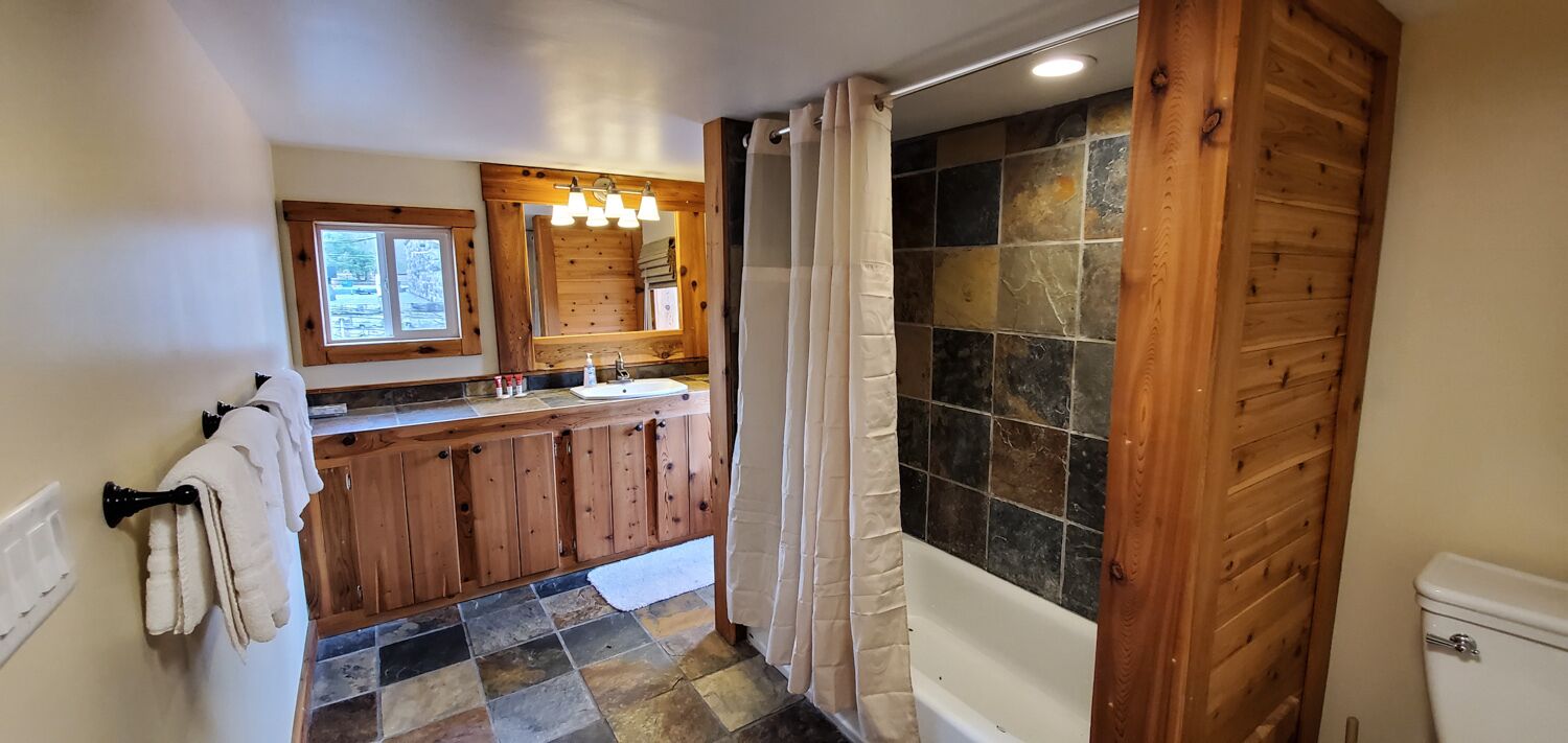 A bathroom with a wooden vanity, a shower with a stone wall, and a toilet.