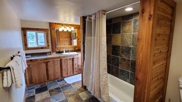 A bathroom with a wooden vanity, a shower with a stone wall, and a toilet.