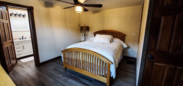 A bedroom with a wooden bed, a ceiling fan, a nightstand, and a dresser.