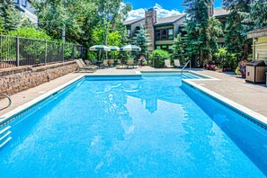 Relax by the pool surrounded by lush greenery and trees, with lounge chairs and umbrellas at your disposal.