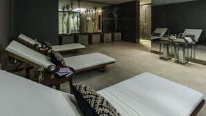 Um spa moderno com várias mesas de massagem, um pequeno balcão de recepção e uma grande janela com plantas.