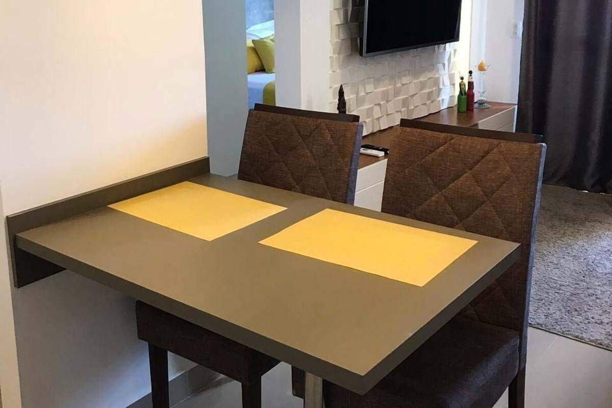 Un espace repas moderne avec une table et des chaises, un téléviseur fixé à un mur texturé et une suspension au-dessus de la table.