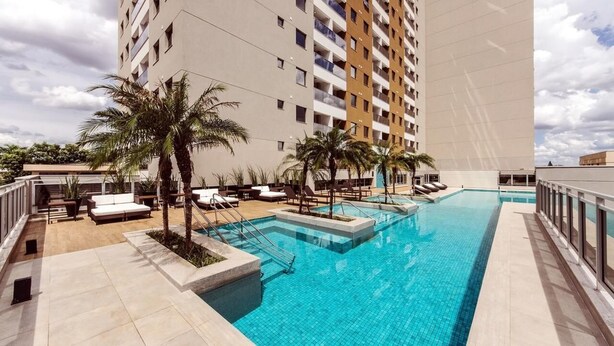 Uma área de piscina com espreguiçadeiras e palmeiras, cercada por edifícios altos.
