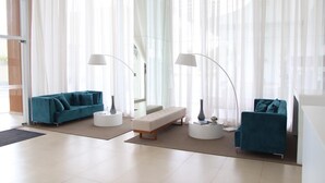 Uma sala de estar moderna com dois sofás verde-água, um banco branco e duas mesas laterais brancas com abajures.