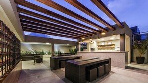 Área de cozinha externa com pergolado, balcão de bar e assentos.