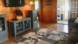 Olohuone, jossa on seinälle asennettu televisio, lasiovilla varustettu kaappi, koristeellinen lamppu ja kuviollinen matto.