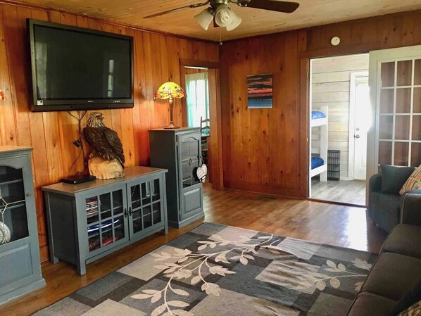 A living room with a television mounted on the wall, a cabinet with glass doors, a decorative lamp, and a patterned rug.