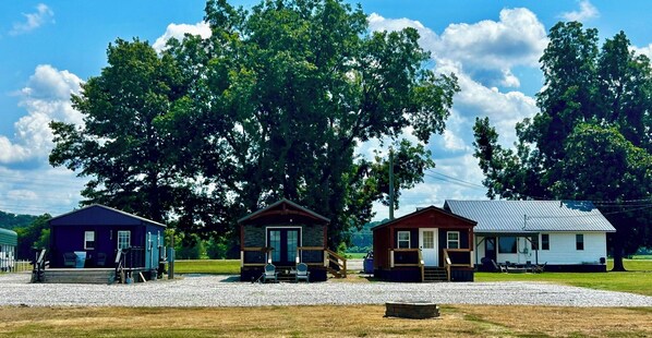 Trois cabanes avec une allée de gravier et de grands arbres en arrière-plan.