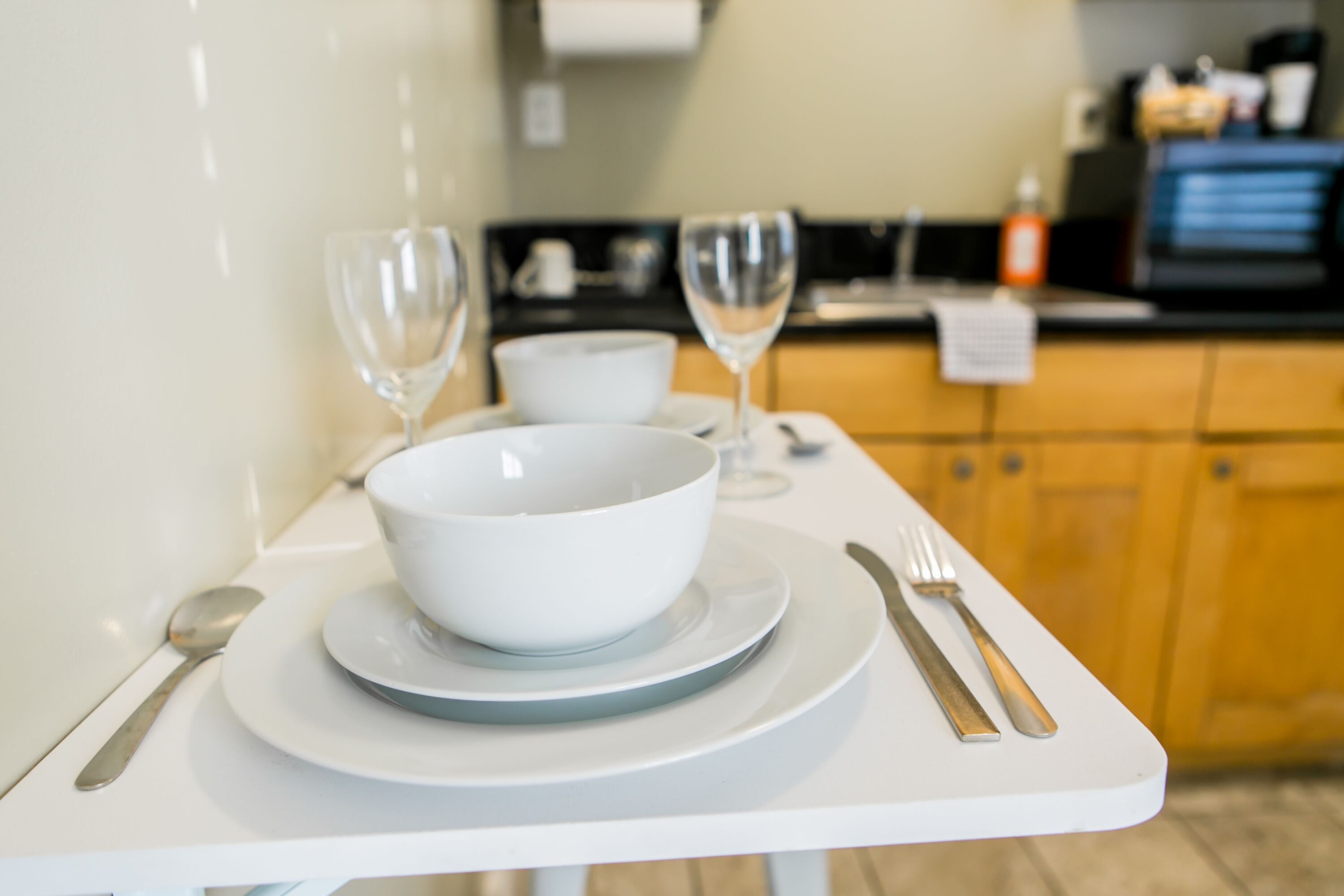 A table set with a white bowl, two wine glasses, a spoon, and a fork.