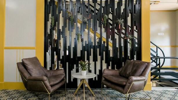 Un interior moderno con dos sillones de cuero, una mesita redonda con planta en maceta y un panel decorativo blanco y negro vertical.