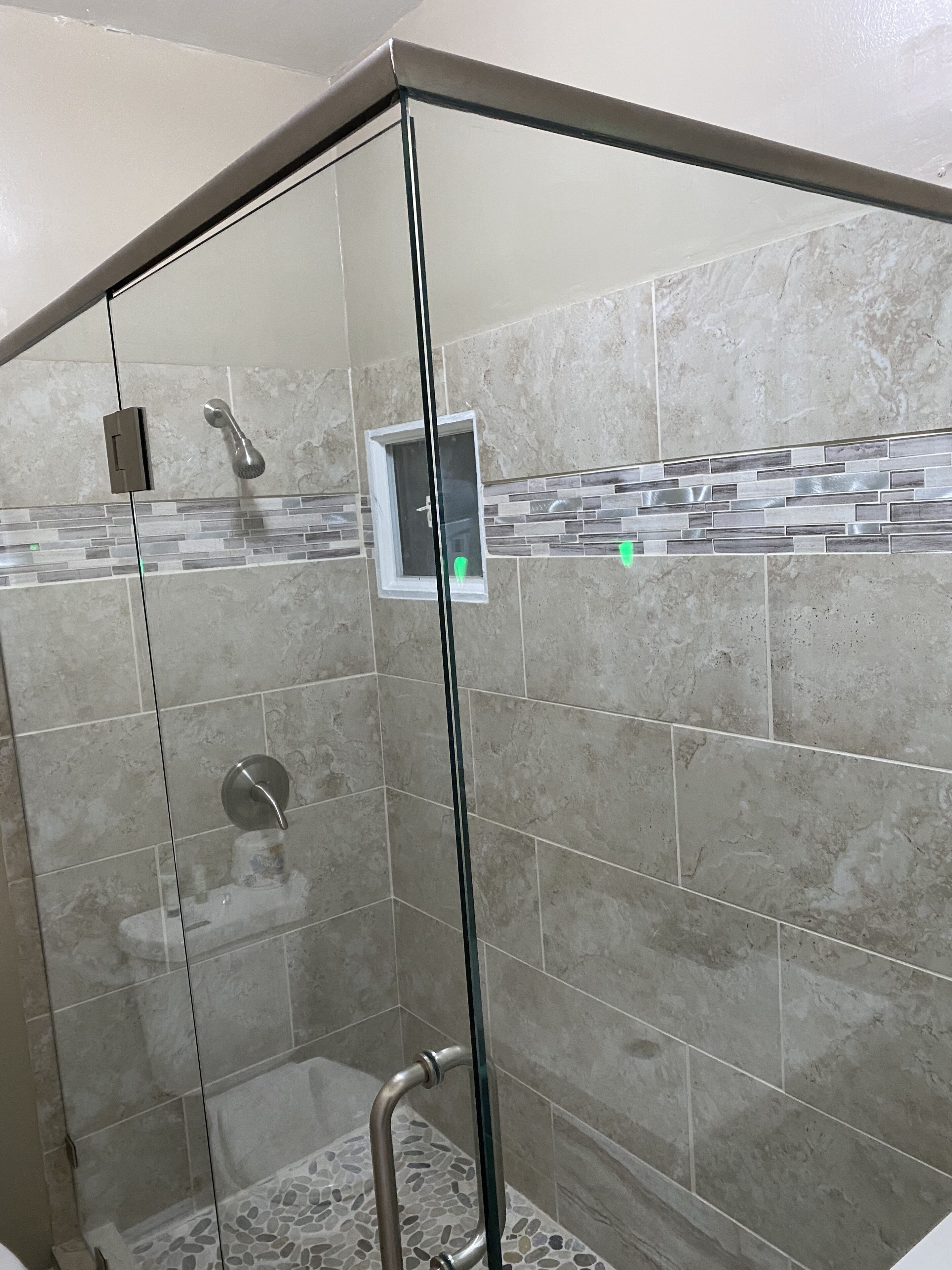 A glass-enclosed shower with a handheld showerhead and a control panel.