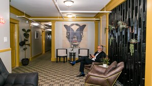 Un vestíbulo de hotel con piso estampado, un gran mural en la pared y una zona de estar con un sillón de cuero marrón y un sofá negro.