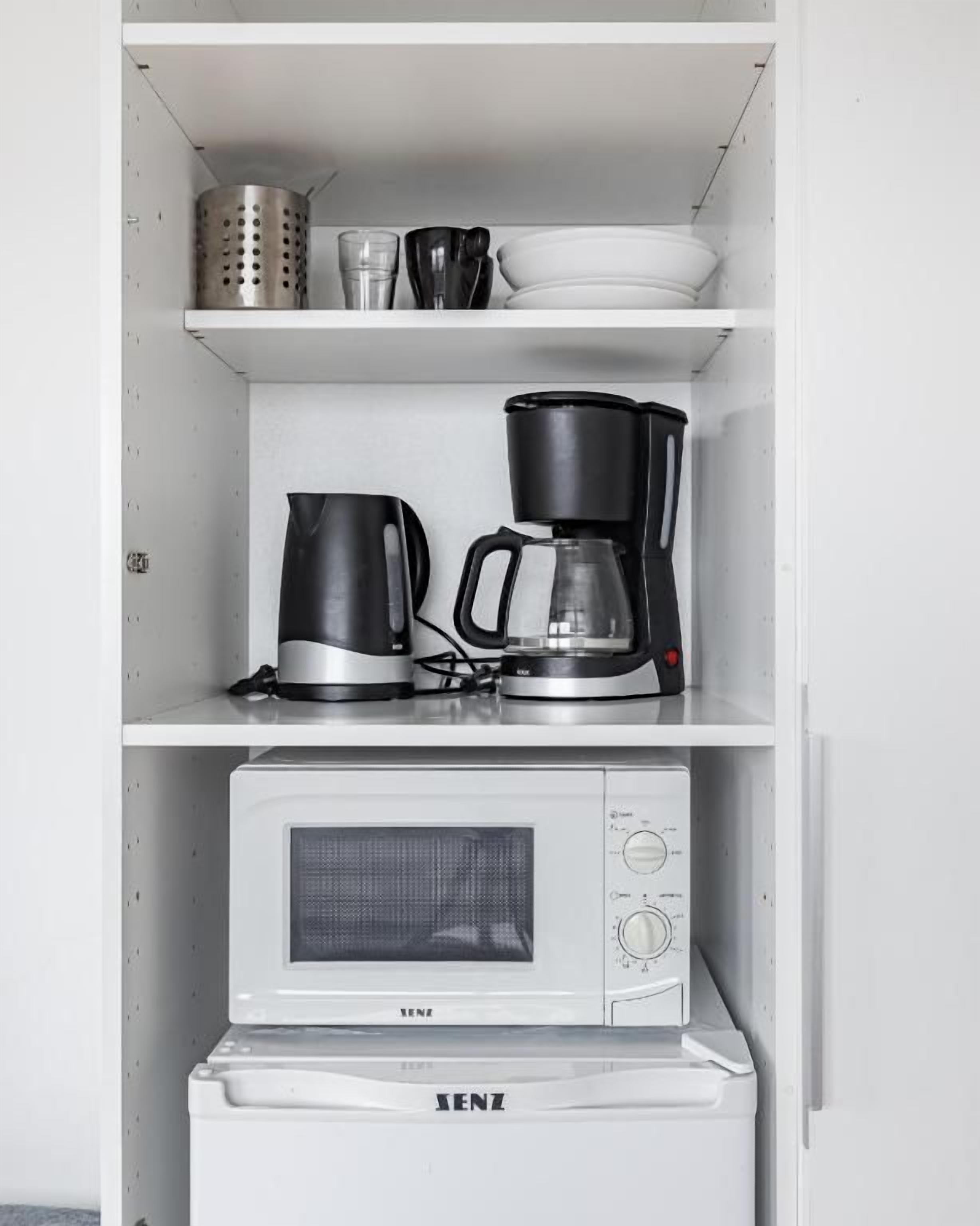 A kitchen with a microwave, coffee maker, and kettle on a white shelf.