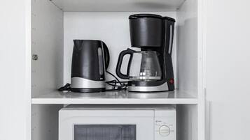 A kitchen with a microwave, coffee maker, and kettle on a white shelf.