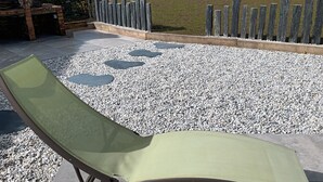 Un patio con una silla lounge verde, un sendero de piedra y una valla de madera.