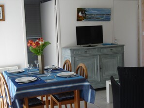 A dining area with a table set for four, a vase with flowers, and a television on a cabinet.