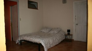 Un dormitorio con una cama, una mesita de noche con una lámpara, una puerta y una lámpara de pared.