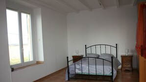 Un dormitorio con estructura de cama metálica, una ventana con vistas y una mesita de noche con lámpara.