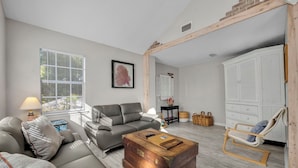 A modern living room with a grey sofa, a wooden coffee table, a rocking chair, and a large wardrobe.