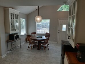 Cozy dining area with a round table and four chairs, kitchenette featuring a microwave and coffee maker, and large windows offering a view of the outside.