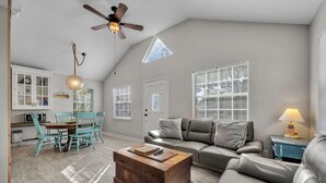 A spacious living room with a high ceiling, a dining area with turquoise chairs, a gray sofa, and a wooden coffee table.