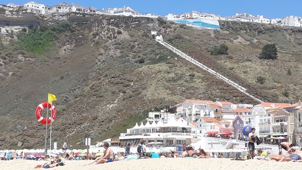 Une ville côtière avec des bâtiments construits sur une colline, une bouée de sauvetage sur la plage et des gens qui se détendent.