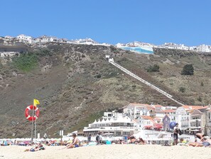 A coastal town with buildings on a hillside, a lifebuoy on the beach, and people relaxing.