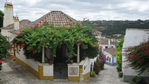 Une rue pavée mène à un bâtiment doté d’un toit en tuiles et d’une enseigne indiquant qu’il s’agit d’une maison d’hôtes.