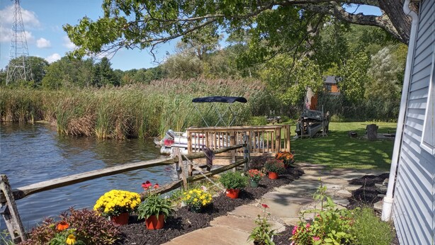 A garden with a stone pathway leading to a wooden deck by a pond, surrounded by various potted plants and flowers. - Lakefront  Fall Foliage in New England Just 2 Hours From NYC (Sharon)