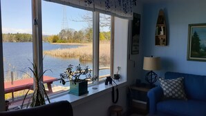 A room with a large window overlooking a lake, a blue couch, a small table, and a lamp. - Lakefront  Fall Foliage in New England Just 2 Hours From NYC (Sharon)