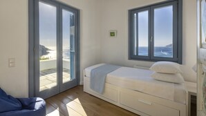 Une chambre à coucher comprenant un lit, une chaise et une porte-fenêtre coulissante donnant sur un balcon avec vue sur la mer.