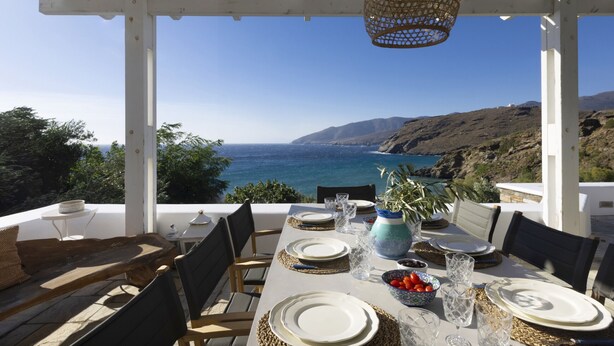 Un coin repas avec une table dressée pour quatre personnes, donnant sur un paysage côtier.
