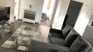 A modern living room with a glass coffee table, grey sofa, and a TV on a stand. - ELD1 - Large 2 bedrooms, Complimentary Netflix & Parking (Peterborough)