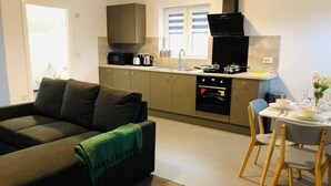 A modern kitchen with a built-in oven, a dining table with chairs, and a sofa with a green throw blanket. - ELD1 - Large 2 bedrooms, Complimentary Netflix & Parking (Peterborough)