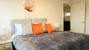 A bedroom with a large bed, two bedside tables, and a door leading to another room. - ELD1 - Large 2 bedrooms, Complimentary Netflix & Parking (Peterborough)
