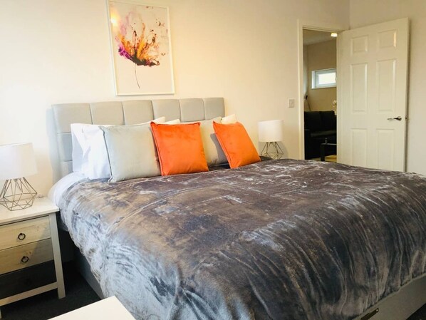 Quarto com cama grande, duas mesas de cabeceira e porta para outro cômodo.