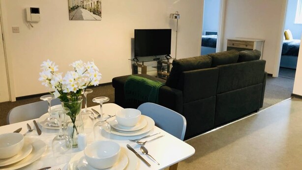 A dining area with a table set for four, a sofa, and a television in the background. - ELD1 - Large 2 bedrooms, Complimentary Netflix & Parking (Peterborough)
