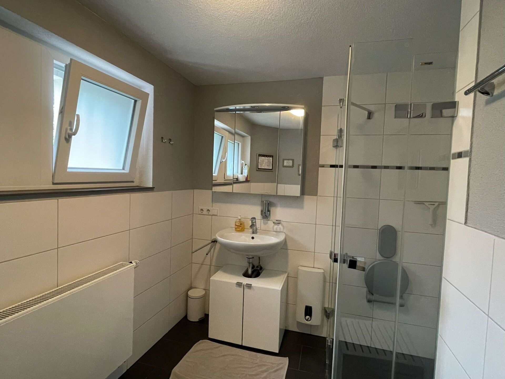 Un bagno con finestra, lavandino, specchio, WC e zona doccia.