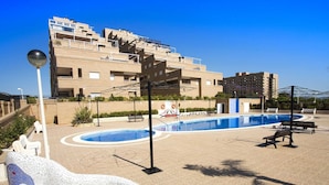 Uma área de piscina com uma obra de arte em mosaico, bancos e um edifício ao fundo.