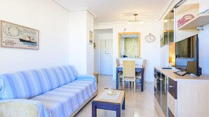 Uma sala de estar moderna com um sofá listrado, uma pequena mesa de madeira e uma área de cozinha com forno embutido e micro-ondas.