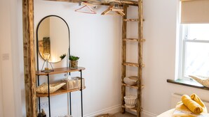 Una habitación con una escalera de madera, un espejo, una estantería con cestas y una cama con toallas amarillas.