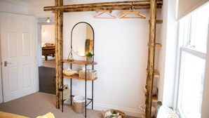 Una habitación con estructura de vigas de madera, un espejo, estantes con cestas y una ventana.