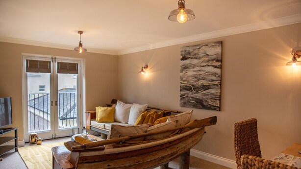 Una sala de estar con una mesa de centro con forma de barco, un sofá con cojines, un cuadro en la pared y un televisor sobre un mueble.