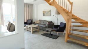 A modern living room with a sofa, chairs, a coffee table, and a wooden staircase. - Lovely apartment in villa for 8 people with WIFI, TV, terrace and pets allowed (Obernsees)
