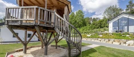 A wooden deck structure with a spiral staircase, surrounded by a landscaped garden and a modern building in the background.