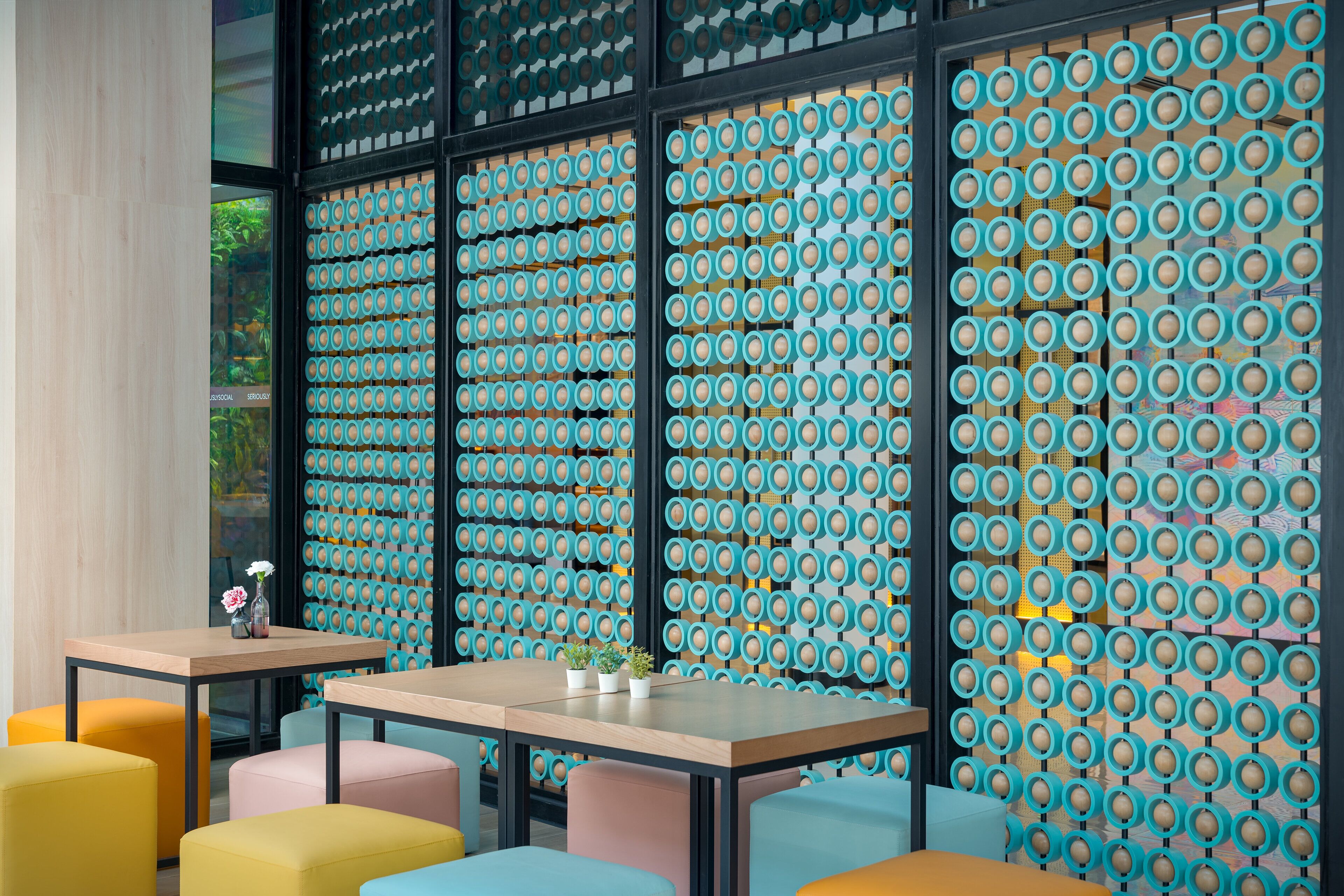 A modern interior with a patterned wall, a wooden table, and colorful seating.